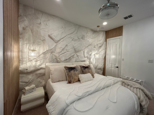 A Bedroom With White Bed and White Side Table. Behind the Bed, The Large White Andes Panel Covers the Wall