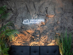 Cavern Rock Wall Panel Mounted to Wall Behind Black Couch. Accent Plants Cover sides of couch