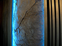 Interior Accent Wall covered by Slate Wall Panel. Black Wood Slats and Blue Light enjoin each Side of Panel
